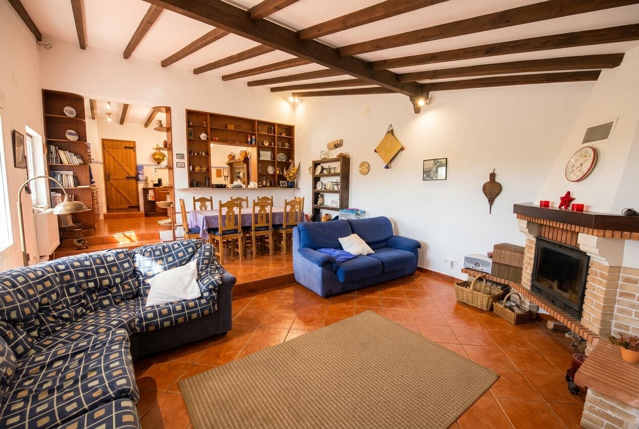Uma sala de estar com sofá, poltrona azul, lareira e área de cozinha ao fundo.