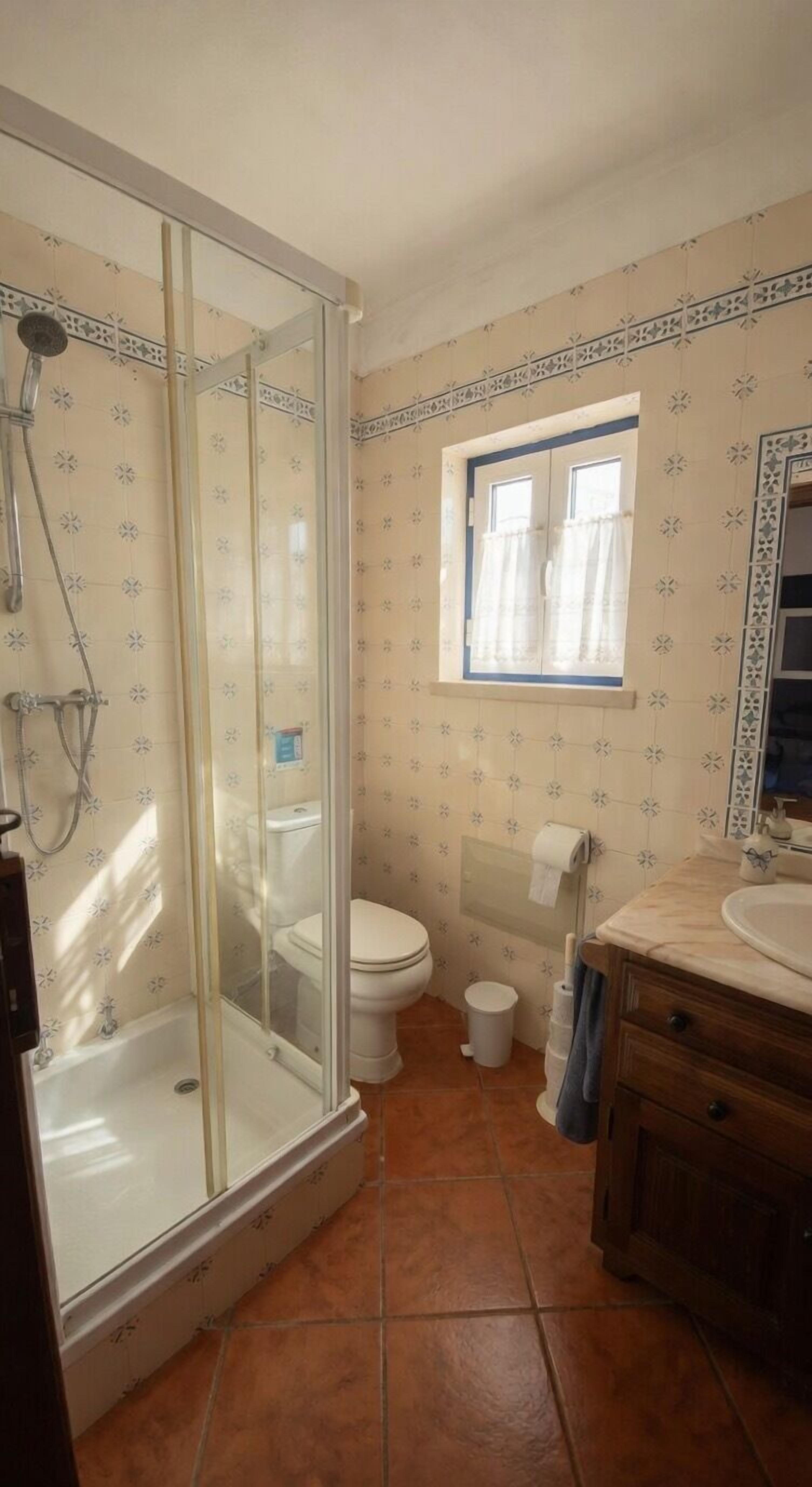 A bathroom with a glass-enclosed shower, a toilet, a sink, and a window.