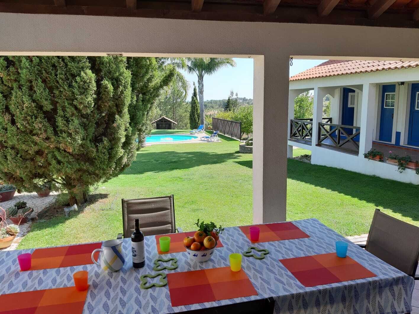 Ein Essbereich im Freien mit Tisch für zwei Personen, mit Blick auf einen Swimmingpool und ein Haus mit blauen Türen.
