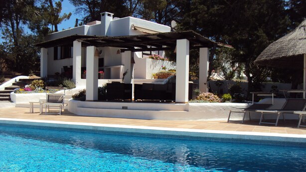 Une piscine avec des chaises longues et un espace salon abrité.