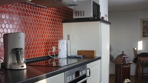 A kitchen with white cabinets, a red patterned backsplash, a coffee maker, a microwave, and a stove.