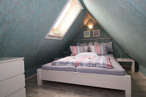 A bedroom with a sloped ceiling, a skylight, a bed with striped bedding, a bedside table, and a dresser.