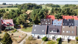 Een woonwijk met meerdere huizen, waarvan sommige rode en andere grijze daken hebben. Er is een speeltuin met een schommel en een glijbaan. Het gebied wordt omringd door bomen en velden.