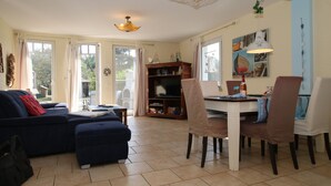 Een woonkamer met een bank, een voetenbankje en een eethoek met stoelen en een tafel.