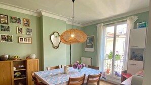 A dining area with a table set for four, wooden chairs, a woven ceiling light, and a view of the outside through a sliding glass door. - Large Family Apartment in Paris (Paris)