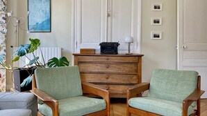 A room with two green upholstered chairs, a wooden chest of drawers, a vintage typewriter, and a framed picture on the wall. - Large Family Apartment in Paris (Paris)