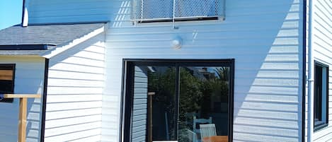 A modern two-story house with a balcony, a sliding glass door, and a wooden deck with outdoor furniture.