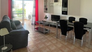 Un saló amb un sofà, una taula de centre, una televisió i una zona de menjador amb cadires i una taula.