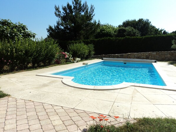 A rectangular swimming pool with a stone wall and a paved deck.