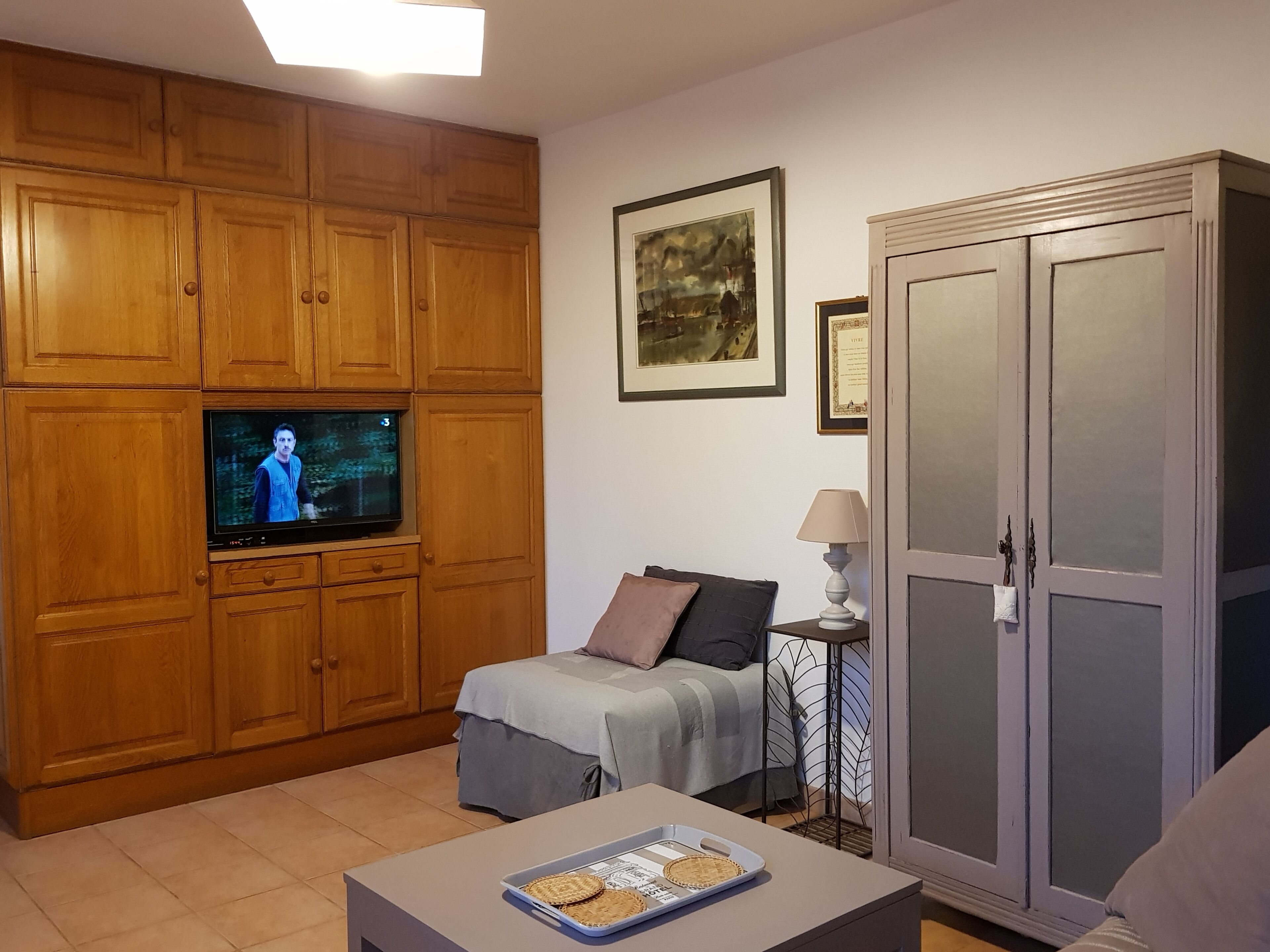 Un salon avec des meubles en bois, un téléviseur, un lit, une table avec un plateau et un meuble de rangement.