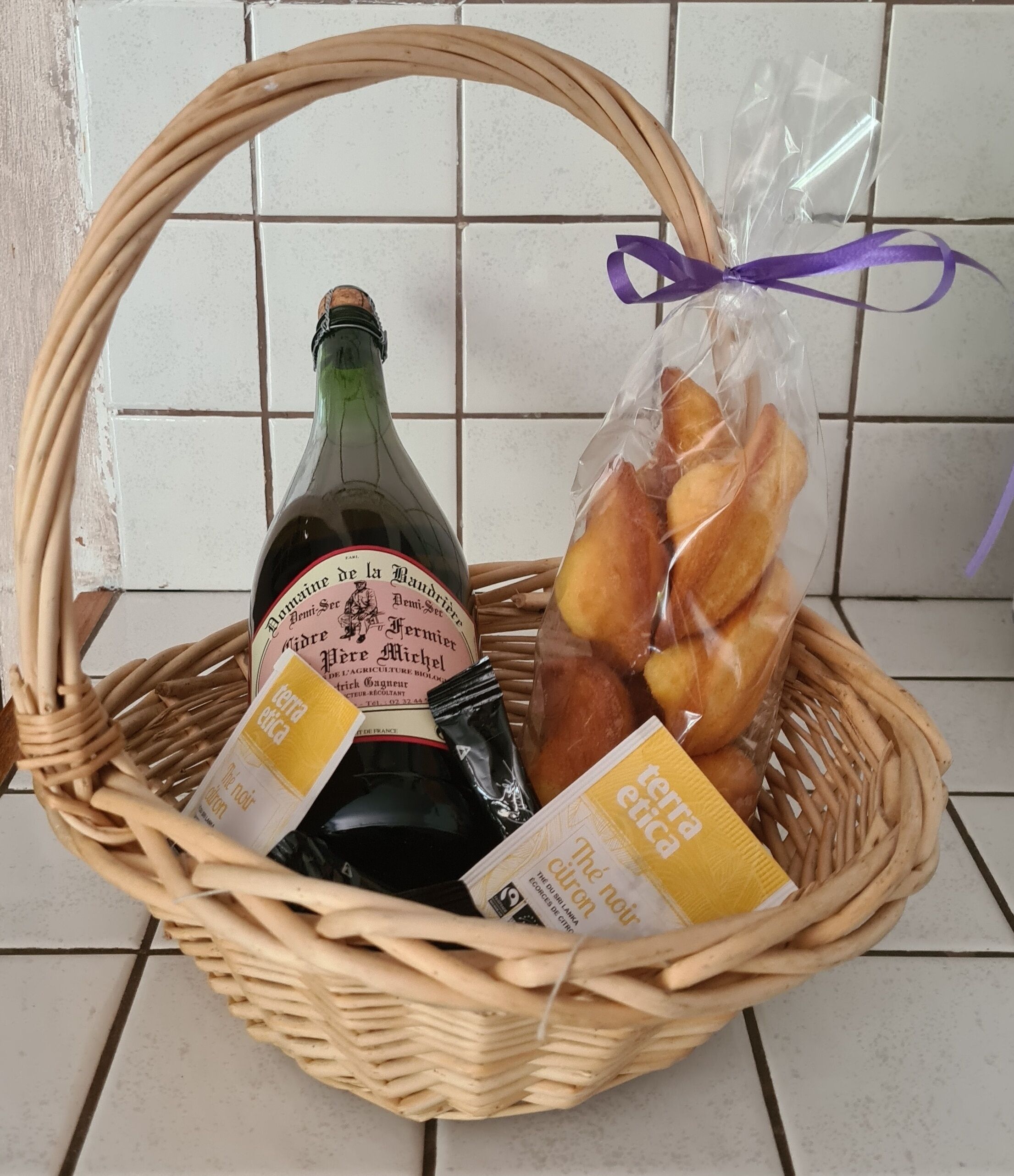 A wicker basket containing a bottle of wine, a bag of bread, and two packets of cheese.