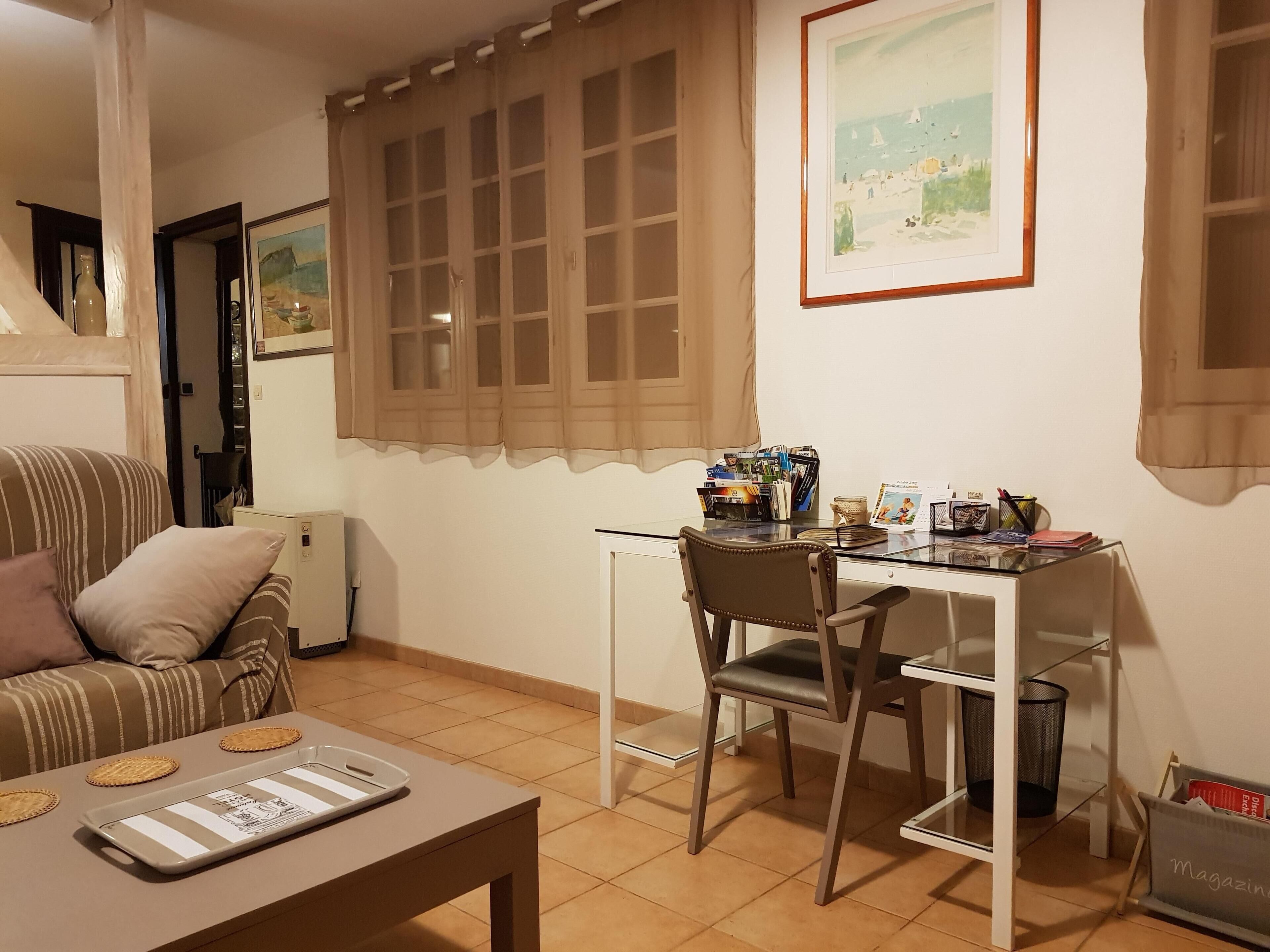 Una sala de estar acogedora con un sofá a rayas, una mesa de comedor con una silla, una ventana con cortina y un cuadro enmarcado en la pared.