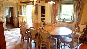 A dining area with a round wooden table surrounded by wicker chairs, a stone wall, and a window with curtains. - House for 10 people, close to the Gulf of Morbihan, Carnac, Trinité-sur-Mer (Brech)