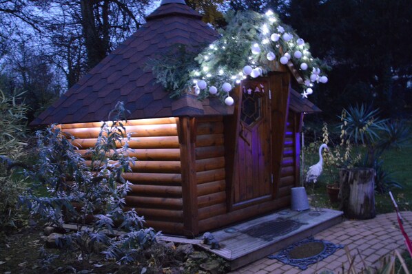 A small wooden cabin with a sloped roof, a door with a decorative panel, and a porch area.