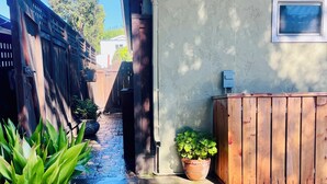 Um beco estreito com piso de concreto, cerca de madeira e um vaso de planta.