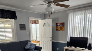Un salon comprenant un canapé, un téléviseur posé sur un meuble, un ventilateur de plafond et une porte avec une fenêtre.