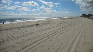Une vaste plage de sable, parsemée d’empreintes de pas et de traces de pneus, un ciel dégagé et une côte lointaine.