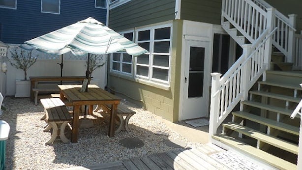 Un bâtiment à deux étages doté d’une terrasse en bois, d’un escalier et d’une table avec un parasol.