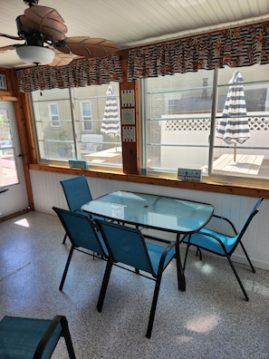 Une pièce avec une table et des chaises, un ventilateur de plafond, une fenêtre avec des rideaux et une vue sur l’extérieur.