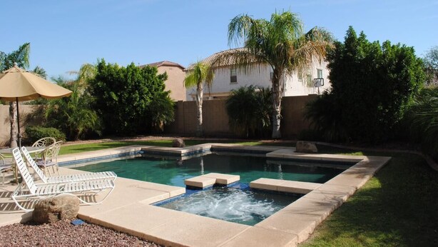 A swimming pool with lounge chairs and a hot tub, surrounded by palm trees and a building.