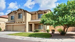 A two-story residential building with a garage, a well-maintained lawn, and a mature tree.