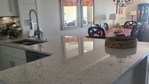 A kitchen with a granite countertop, a sink, and a dining area with chairs and a table.