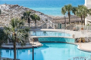 Une piscine au design incurvé, entourée de palmiers et offrant une vue sur l’océan.