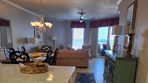 A kitchen with a granite countertop, a dining area with a table and chairs, a sofa, and a view of the ocean through large windows.