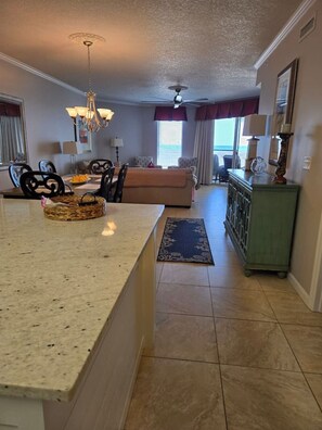 A kitchen with a granite countertop, a dining area with a table and chairs, a sofa, and a view of the ocean through large windows. - Enjoy our oasis of relaxation & beautiful beaches (Santa Rosa Beach)