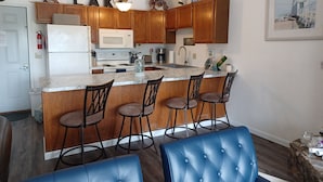 A modern kitchen with wooden cabinets, a marble countertop, and a bar area with stools.