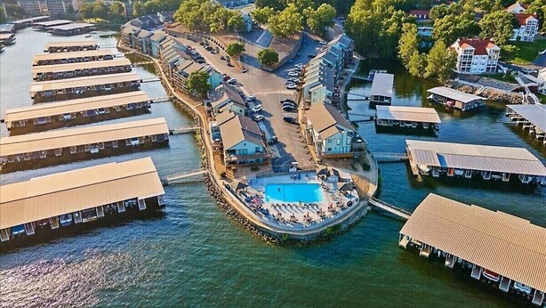 An aerial view of a waterfront property with multiple floating structures, a central swimming area, and a surrounding road.