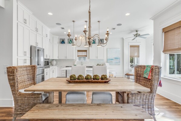 A spacious kitchen with white cabinets, a wooden dining table, wicker chairs, and a chandelier.
