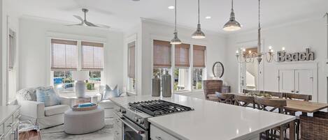 A modern kitchen with a central island, white cabinetry, and a dining area with wooden chairs and a chandelier.