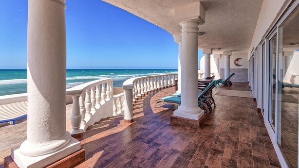 A covered balcony with white columns, a wooden floor, and a view of the ocean.