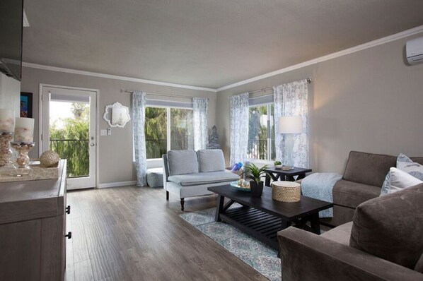 A spacious living room with a grey sofa, a coffee table, and a dining area with a dark wooden table.