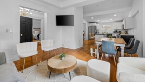 Un amplio salón con una mesa de comedor, sillas y un televisor montado en la pared.