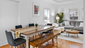 Un comedor con una mesa de madera, bancos y sillas. Hay un sofá y una mesa baja en la sala.