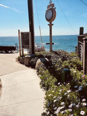 A coastal walkway with a clock, informational sign, and a view of the sea.