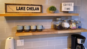 A kitchen with a sign reading "LAKE CHELAN" and another sign saying "COFFEE TIME". There are jars on the shelf, a coffee maker, and a small plant. - Steps to Lakefront Park. Close to Town, Waterslides, Wineries, and Golf Courses. (Chelan)