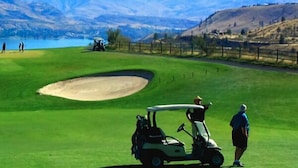 A golf course with a sand bunker, a golf cart, and a person standing nearby. - Steps to Lakefront Park. Close to Town, Waterslides, Wineries, and Golf Courses. (Chelan)