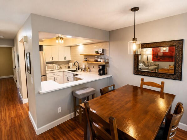 A modern kitchen with white cabinets, a wooden dining table, and a built-in coffee station. - Steps to Lakefront Park. Close to Town, Waterslides, Wineries, and Golf Courses. (Chelan)