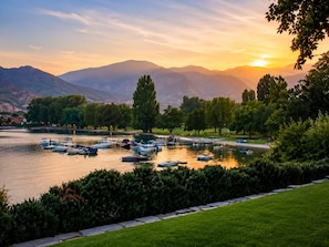 A lakeside view with boats docked, trees, and mountains in the background. - Steps to Lakefront Park. Close to Town, Waterslides, Wineries, and Golf Courses. (Chelan)