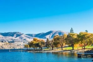 Un parque junto al lago con un muelle, árboles y un paisaje montañoso al fondo.