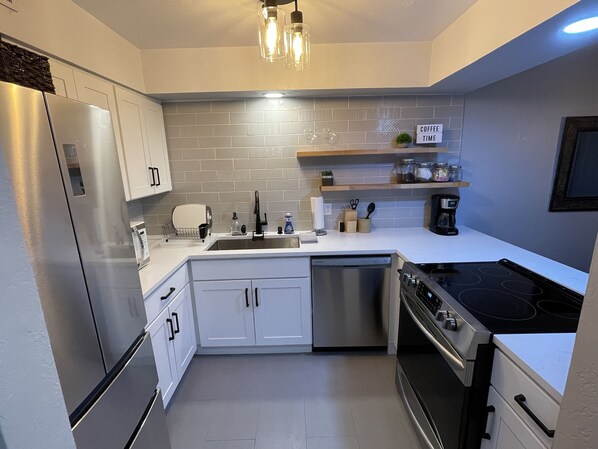 A modern kitchen with stainless steel appliances, white cabinetry, and a tiled backsplash.