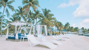 Uma praia com cadeiras de praia brancas e uma estrutura tipo toldo com almofadas azuis.