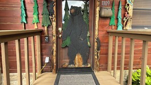 A wooden cabin entrance with a bear sculpture, a mailbox, and a number '1109' on the door.