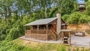 A cabin with a wooden deck, stone chimney, and a covered porch.
