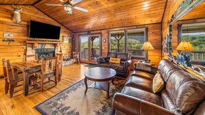 A cabin interior with a wooden ceiling, a fireplace, a TV, a sofa, and a dining area.