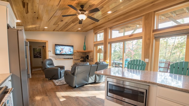 A modern kitchen with a built-in oven, a grey sofa, and a television mounted on the wall. - Silver Lining Cabin -Natural light, Quiet, Hot Tub, Nature Trails, Pet door (Fletcher)
