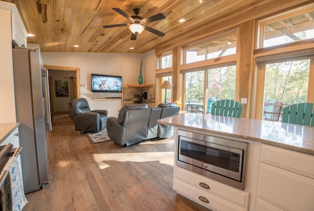 A modern kitchen with a built-in oven, a grey sofa, and a television mounted on the wall.
